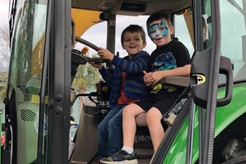 Two young boys sitting behind the wheel of a tractor smiling