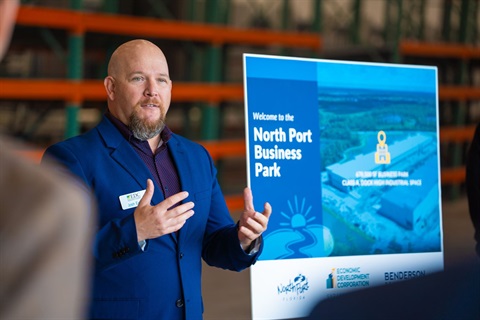 A man speaking to a group in front of a sign that reads 